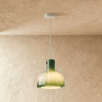 Clérachic green-to-pale-yellow glass pendant with a lobed shade, glowing warm from a white stem against a plaster wall.
