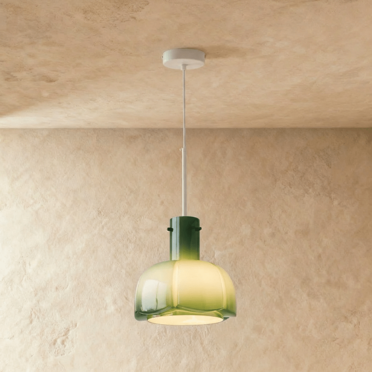 Clérachic green-to-pale-yellow glass pendant with a lobed shade, glowing warm from a white stem against a plaster wall.