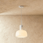Clérachic creamy opal glass pendant with a lobed shade, glowing softly on a slim white stem against a limewashed wall.
