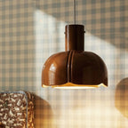 Close-up of the Clérachic glossy brown glass pendant, its ribbed lobed shade lit warm against blue gingham wallpaper.