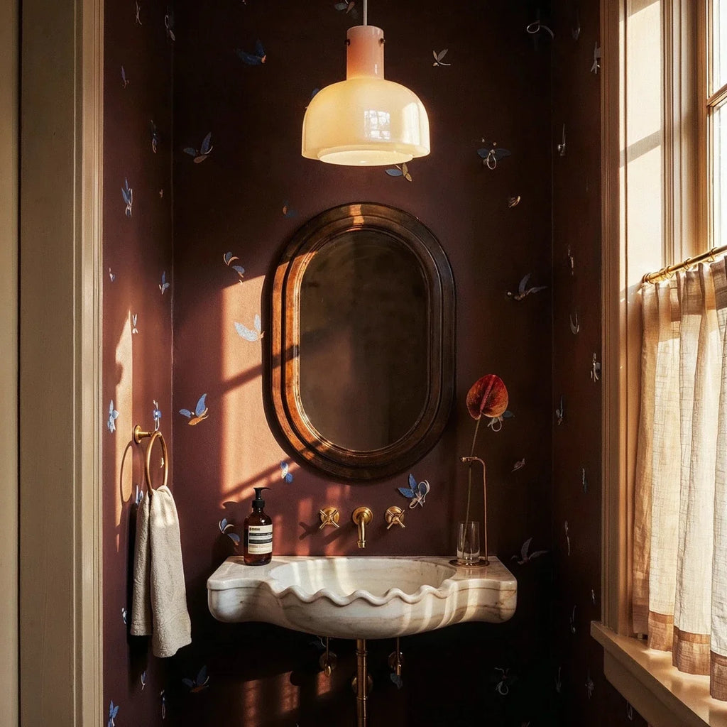 Clérachic pale pink and cream glass pendant lit above an oval mirror and scalloped marble basin in a dark powder room.