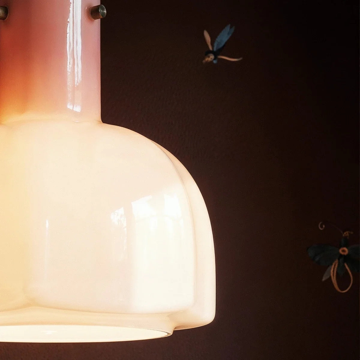 Close-up of the Clérachic pink-to-cream glass pendant shade, lit warm, with brass fixings on its neck.