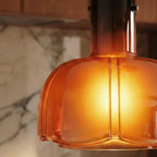 Close-up of the Clérachic amber glass pendant, its lit lobed shade fading to a darker smoked neck with metal pins.