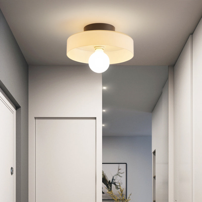 Clérachic coloured glass drum flush mount ceiling light in white, its opal globe bulb lighting a narrow hallway.