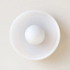 White glass drum flush mount from Clérachic seen head-on, the opal globe centred inside the glossy shade on a pale wall.