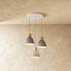 Closer view of the Clérachic three-head grey wood disc pendant light on its round white ceiling canopy over a plaster wall.