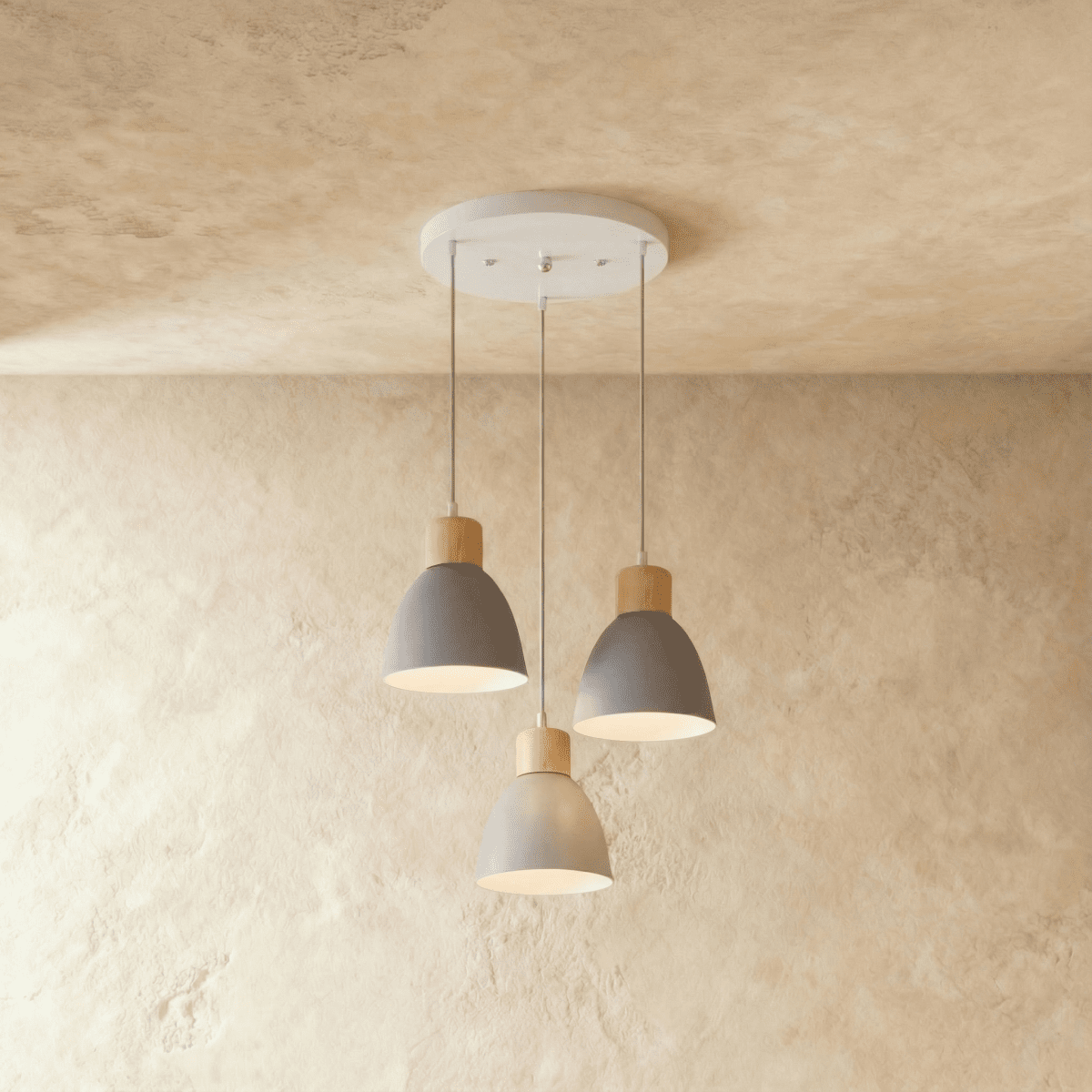 Closer view of the Clérachic three-head grey wood disc pendant light on its round white ceiling canopy over a plaster wall.