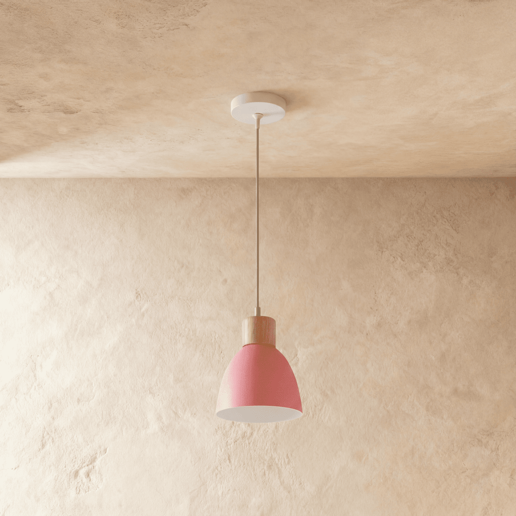 A single Clérachic wood disc pendant light in soft pink hangs on a long cable against a warm plaster backdrop.