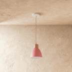 A single Clérachic wood disc pendant light in soft pink hangs on a long cable against a warm plaster backdrop.