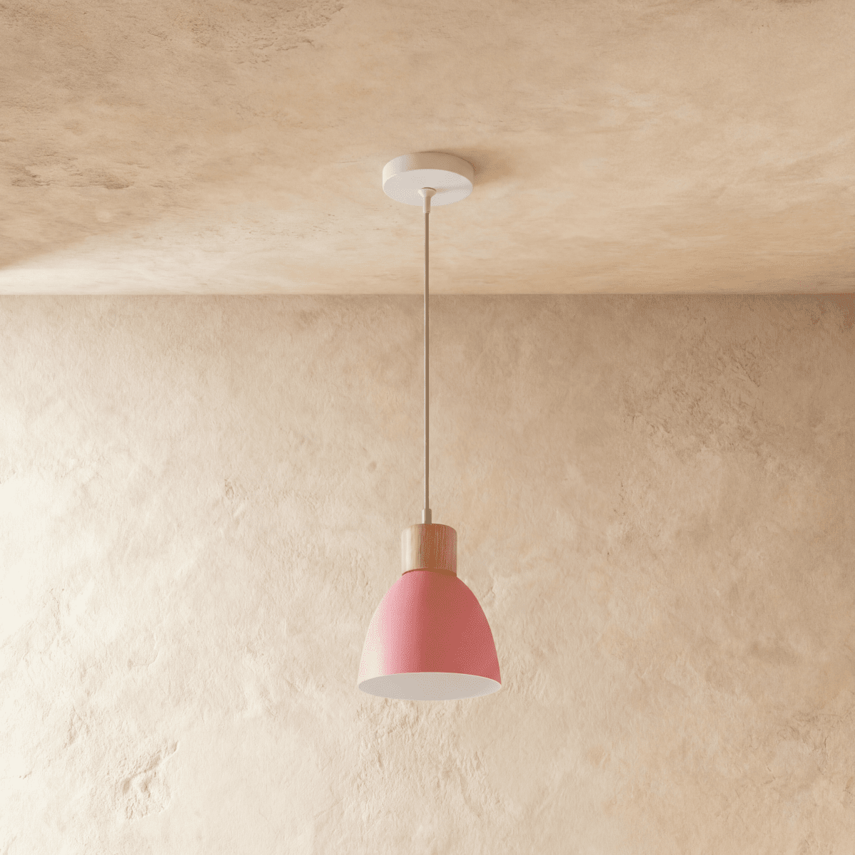 A single Clérachic wood disc pendant light in soft pink hangs on a long cable against a warm plaster backdrop.