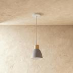 A single Clérachic wood disc pendant light in matte grey hangs on a long cable against a warm plaster backdrop.