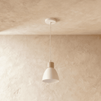 A single Clérachic wood disc pendant light in warm white hangs from a round canopy against a plaster ceiling.