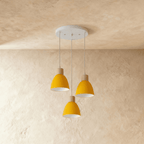 Three Clérachic wood disc pendant lights in mustard yellow cluster from a round canopy against a plaster wall.