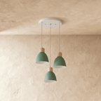 Three Clérachic wood disc pendant lights in sage green cluster from a round canopy against a plaster wall.