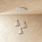 Three Clérachic wood disc pendant lights in warm white cluster from a round canopy over a plaster backdrop.
