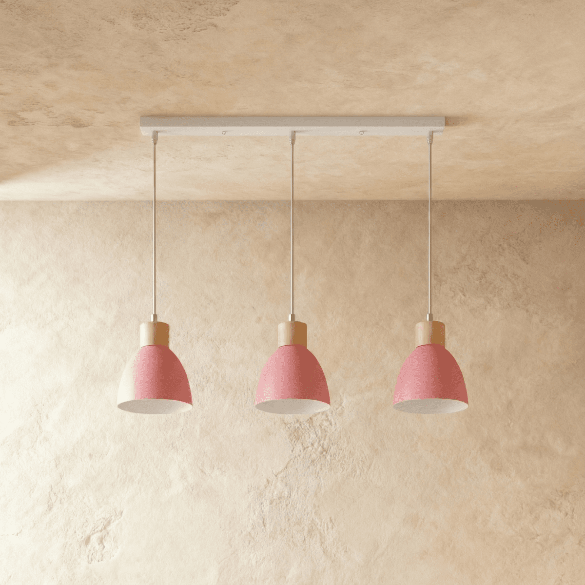 Three Clérachic wood disc pendant lights in soft pink hang in a row from a linear bar for a kitchen island.