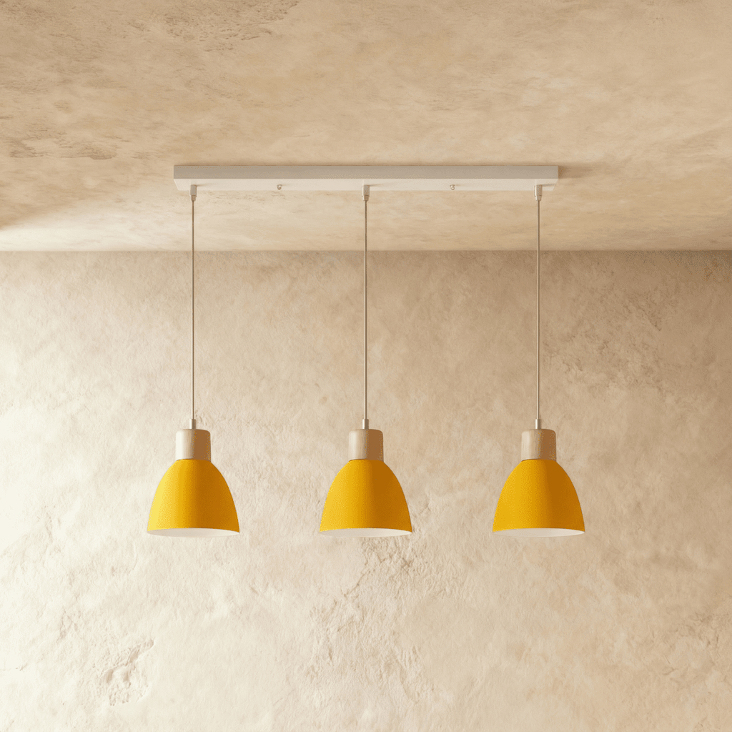 Three Clérachic wood disc pendant lights in mustard yellow hang in a row from a linear bar over a plaster wall.