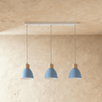 Three Clérachic wood disc pendant lights in dusty blue hang in a row from a linear bar for a kitchen island.
