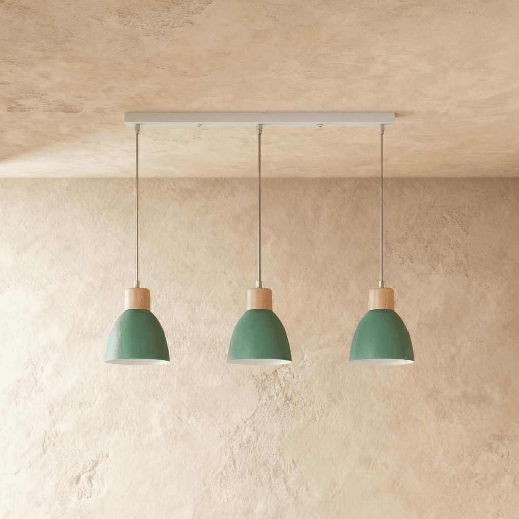 Three Clérachic wood disc pendant lights in sage green hang in a row from a linear bar over a plaster wall.
