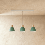 Three Clérachic wood disc pendant lights in sage green hang in a row from a linear bar over a plaster wall.