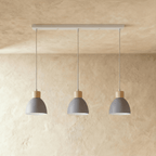Three Clérachic wood disc pendant lights in matte grey hang in a row from a linear bar for a kitchen island.