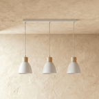 Three Clérachic wood disc pendant lights in warm white hang in a row from a linear bar over a plaster wall.