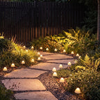Clérachic solar mushroom stake lights line a stone garden path at dusk, warm white caps glowing among ferns and gravel.