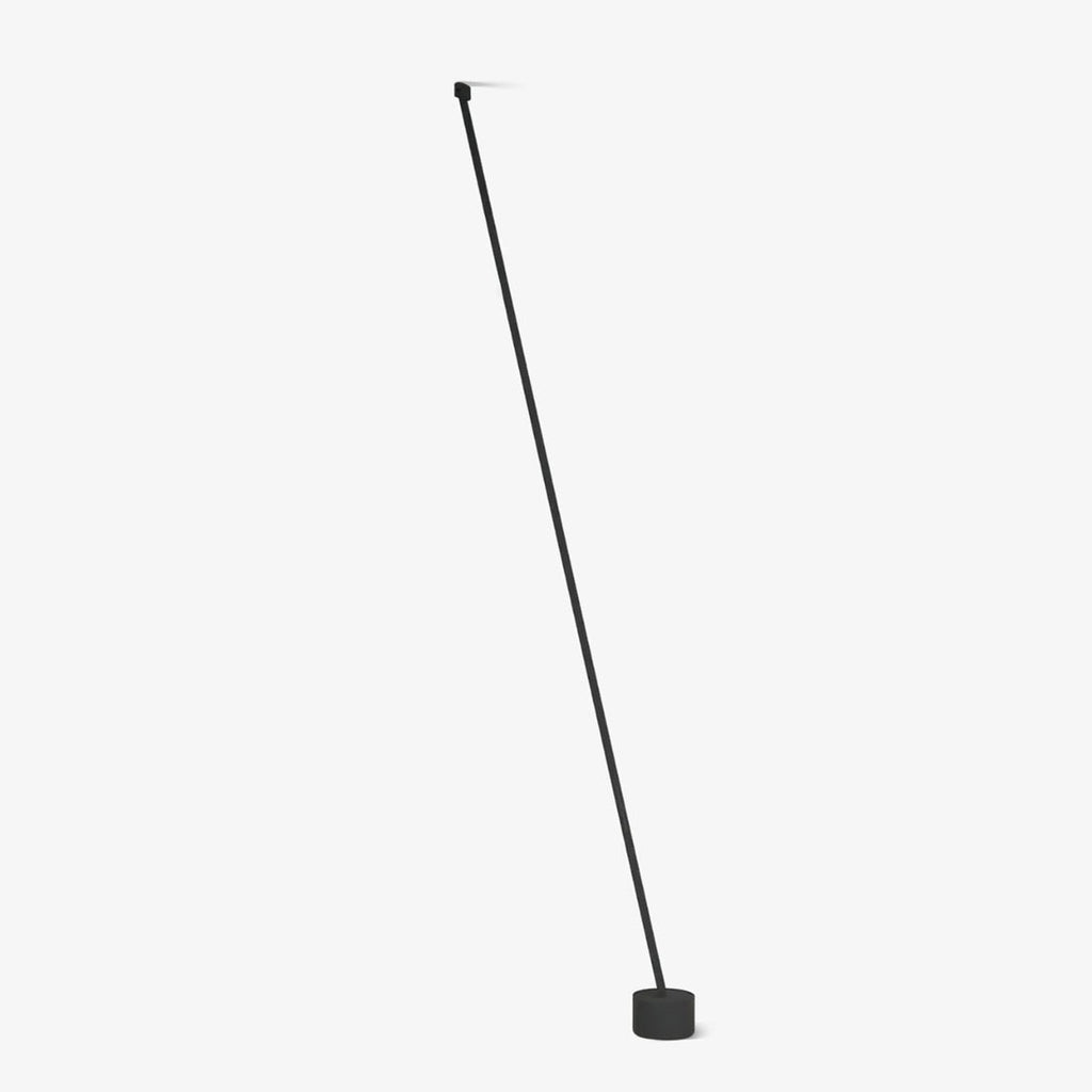 A slim black webbing strip leans from a small ceiling fixing to a round black base on a plain white backdrop, this Clérachic floor lamp unlit.