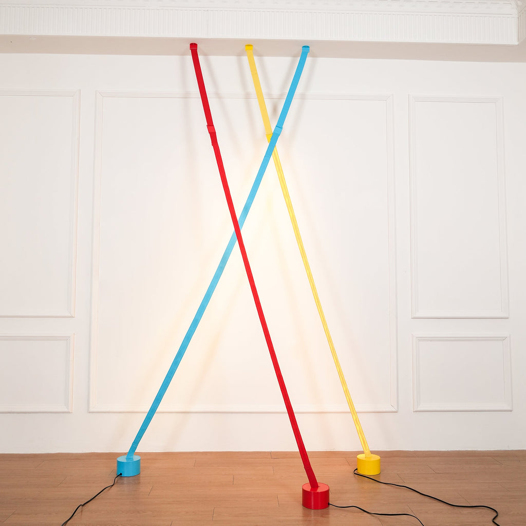 Red, yellow and light blue Clérachic floor lamp strips cross against a white panelled wall, each standing on a matching round base.
