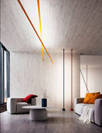 Lit ochre strips of this Clérachic floor lamp angle across a concrete ceiling above a living room with a blue vase and a grey sofa.