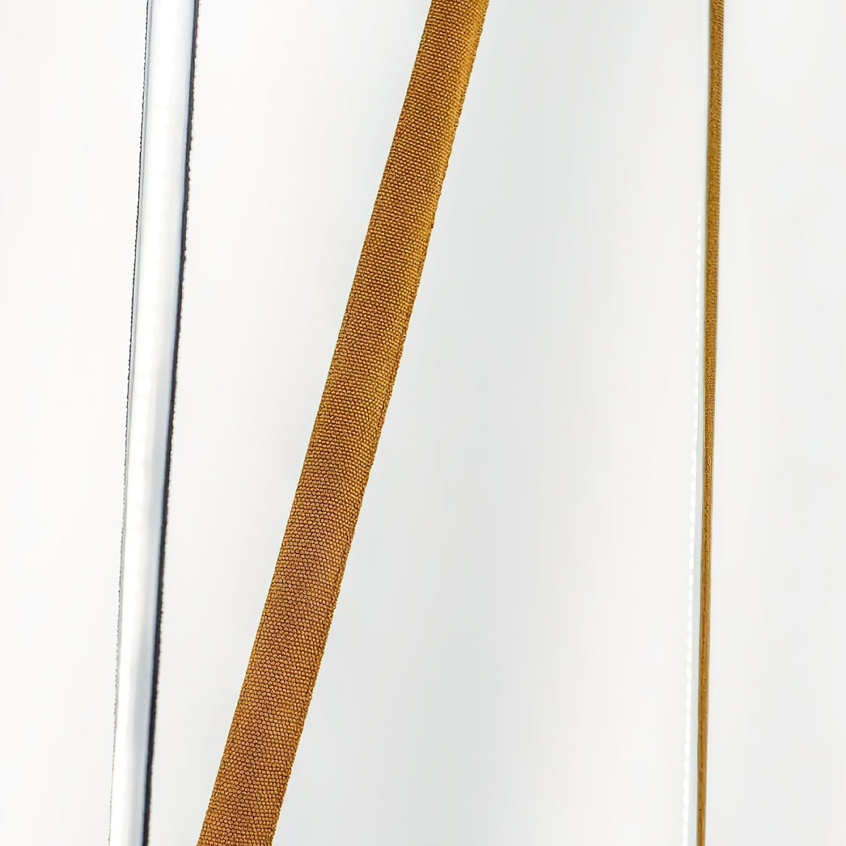 Close view of the woven ochre webbing on a Clérachic floor lamp strip, set against a bright white wall with a lit edge.