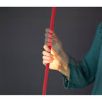 A hand grips a red Clérachic floor lamp strip against a dark grey backdrop, showing how slim and flat the webbing is.