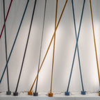 Blue, grey, ochre and black Clérachic floor lamp strips lean against a white wall lit from behind, each on its own round base.