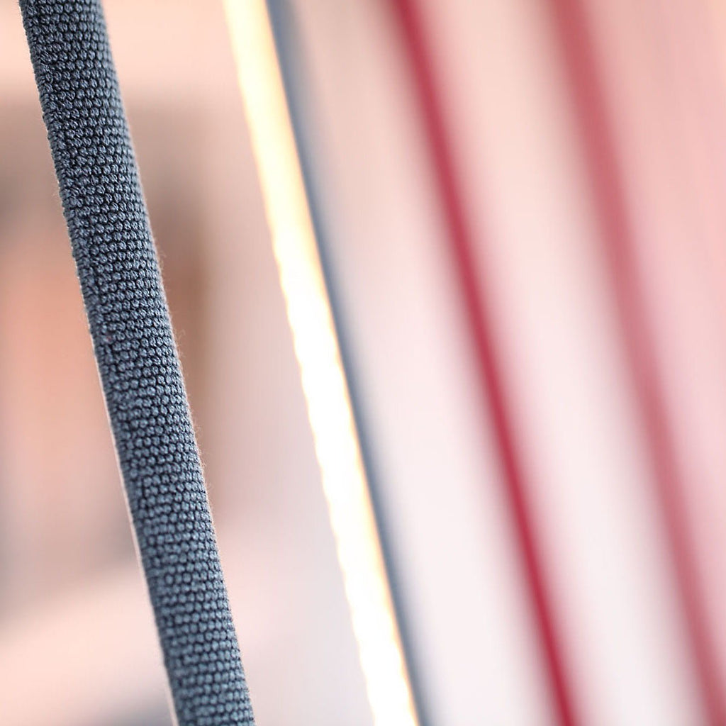Close view of grey-blue knitted webbing beside a bright light line on a Clérachic floor lamp, with red strips blurred behind.
