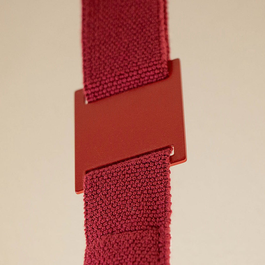 Close view of a red metal sleeve joining two lengths of knitted red webbing on a Clérachic floor lamp, against a beige backdrop.