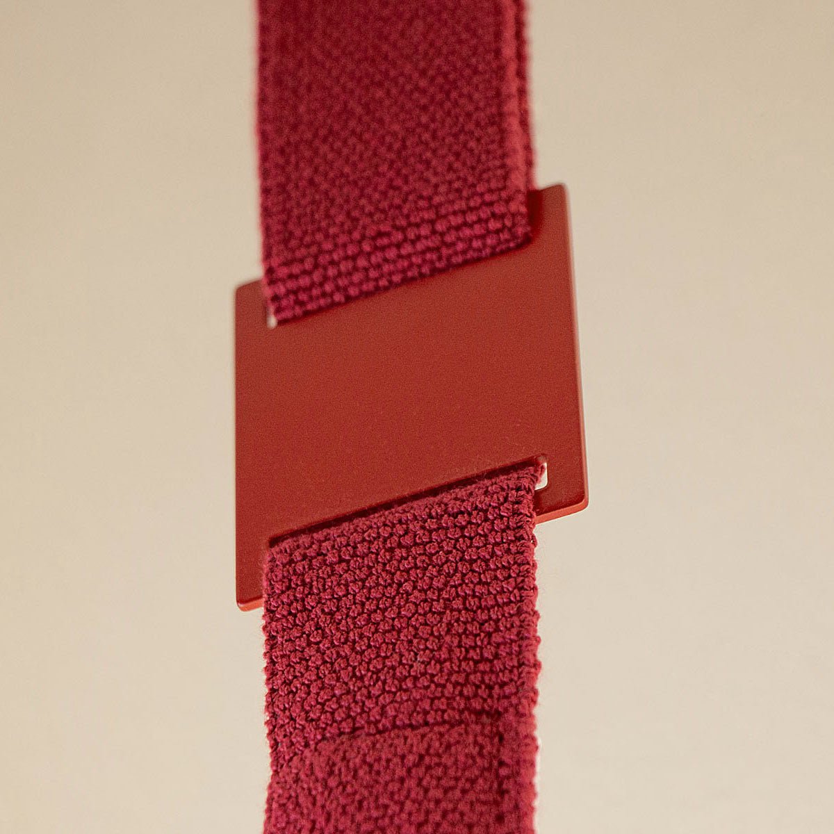 Close view of a red metal sleeve joining two lengths of knitted red webbing on a Clérachic floor lamp, against a beige backdrop.