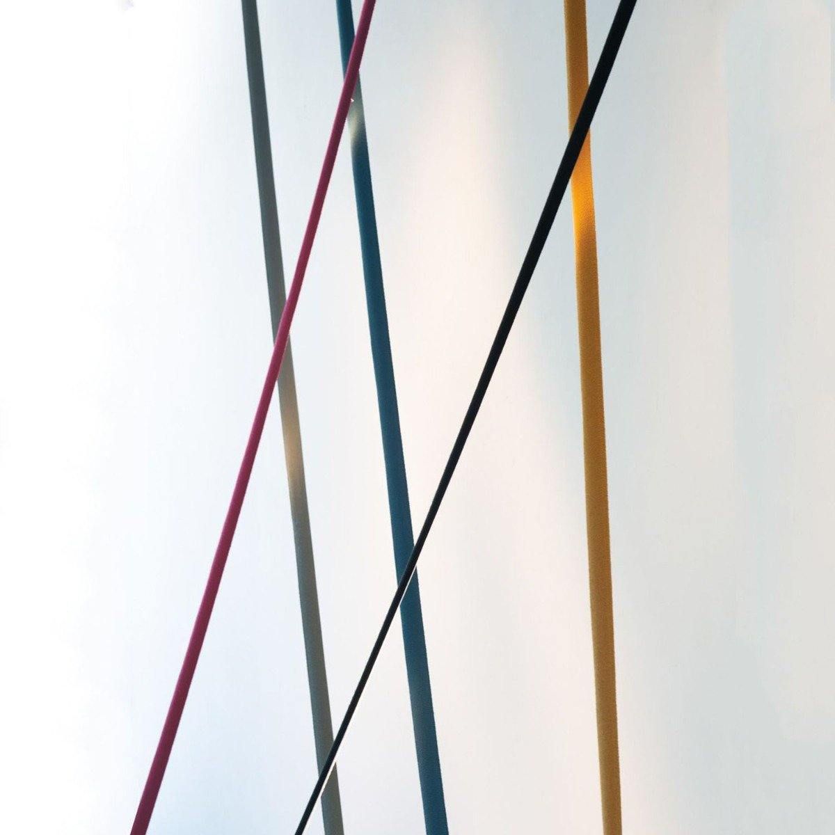 Detail of five Clérachic floor lamp strips in red, grey, blue, black and ochre crossing in front of a softly lit white wall.