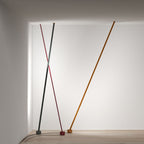 Three Clérachic floor lamp strips in grey, red and ochre lean from the ceiling in a white room, their cords running across a wood floor.