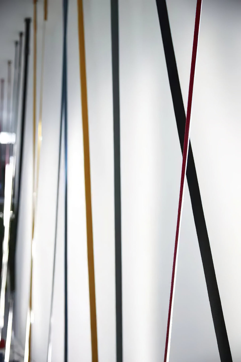 Seen at a low angle, many Clérachic floor lamp strips in black, red, ochre and grey lean along a white wall.