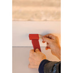 Hands fix a small red bracket to a ceiling edge, showing how the strip of this Clérachic floor lamp attaches at the top.