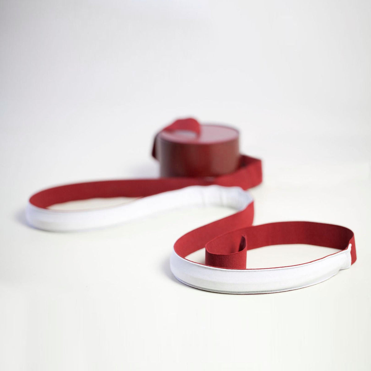 A red webbing strip coils out from its round base across a pale surface, with a white inner backing on this Clérachic floor lamp.
