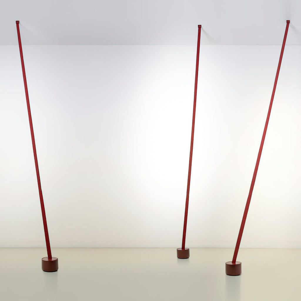 Three red Clérachic floor lamp strips stand at slight angles in a bright white room, each on a dark round base.