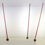Three red Clérachic floor lamp strips stand at slight angles in a bright white room, each on a dark round base.