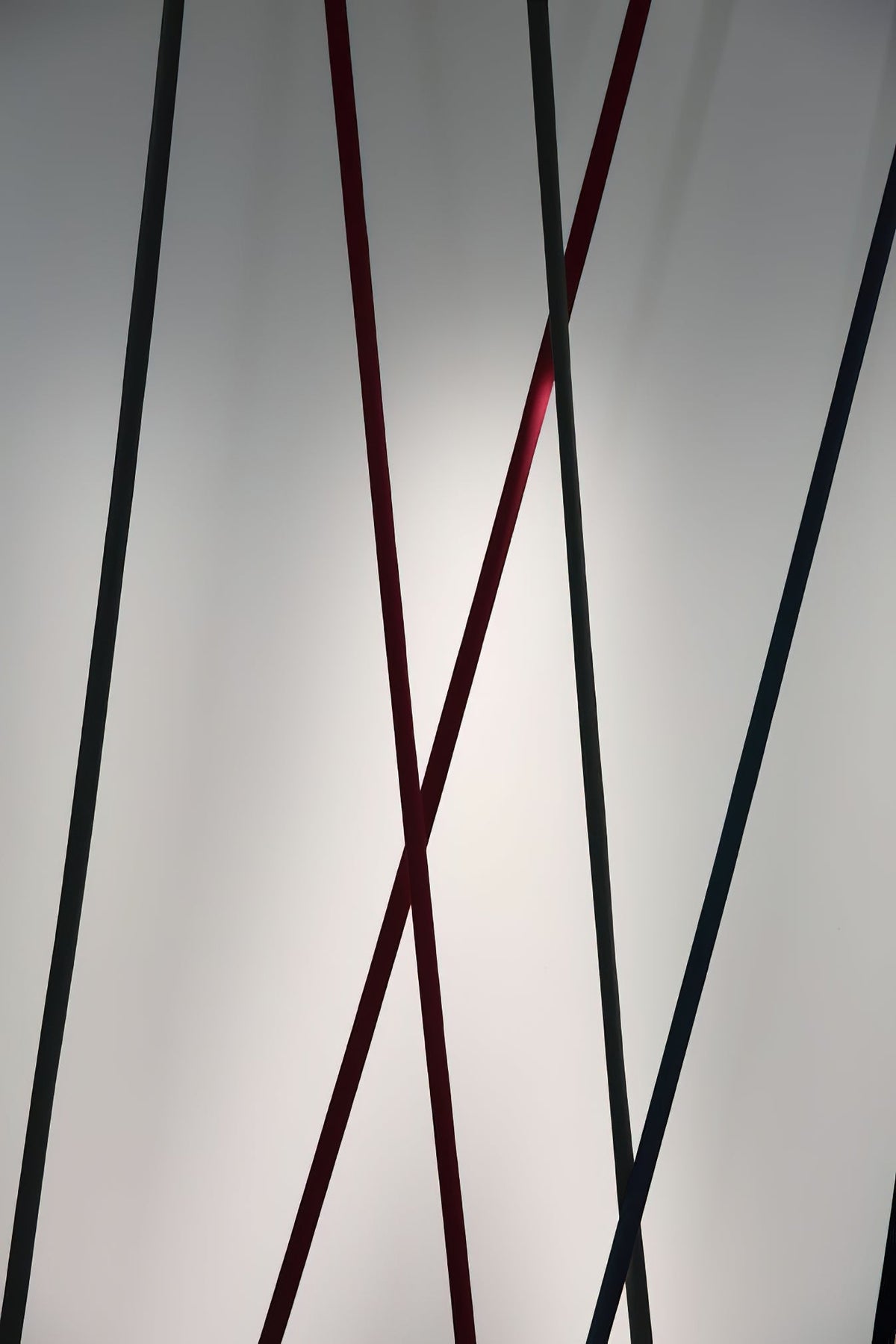 Close view of black and red Clérachic floor lamp strips crossing, in front of a softly lit grey wall.