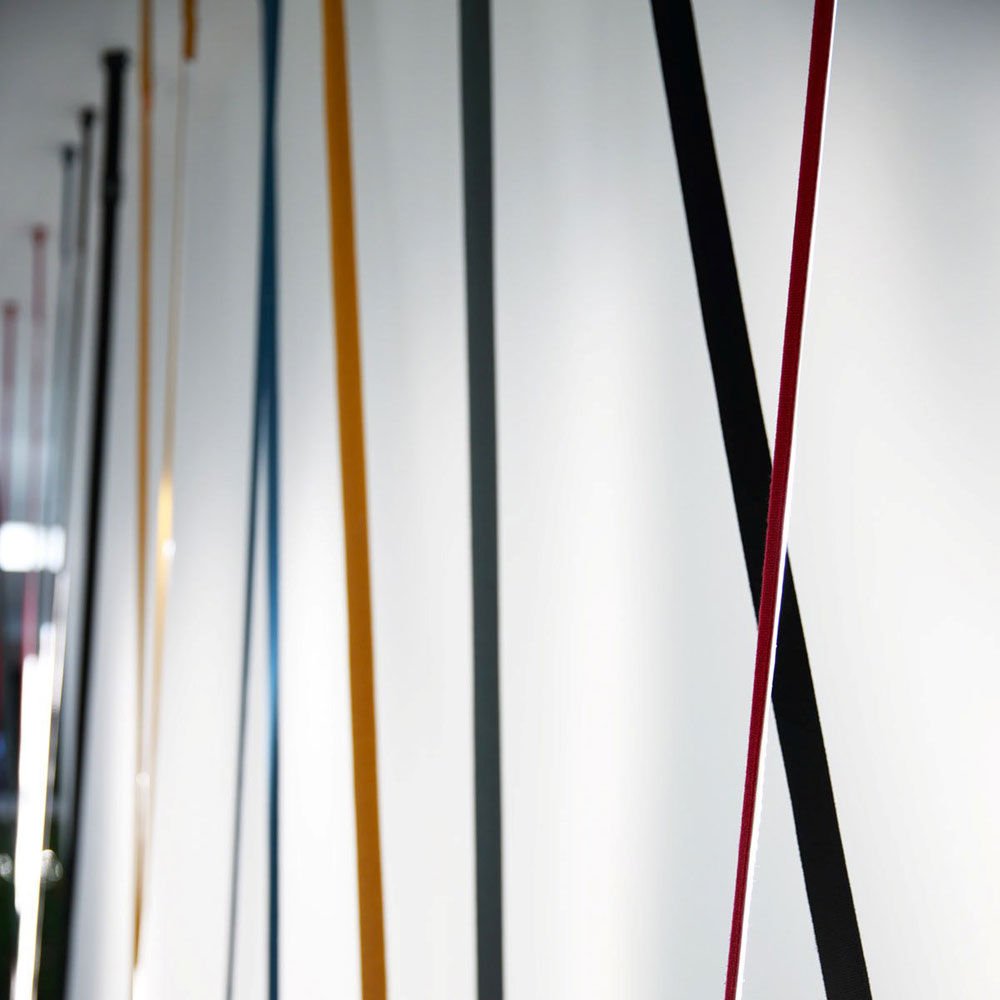 Close view of ochre, grey, black and red Clérachic floor lamp strips running down past each other along a white wall.