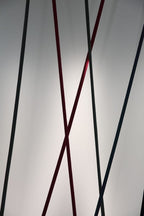 Black, red and dark grey Clérachic floor lamp strips cross at different angles in front of a softly lit grey wall.