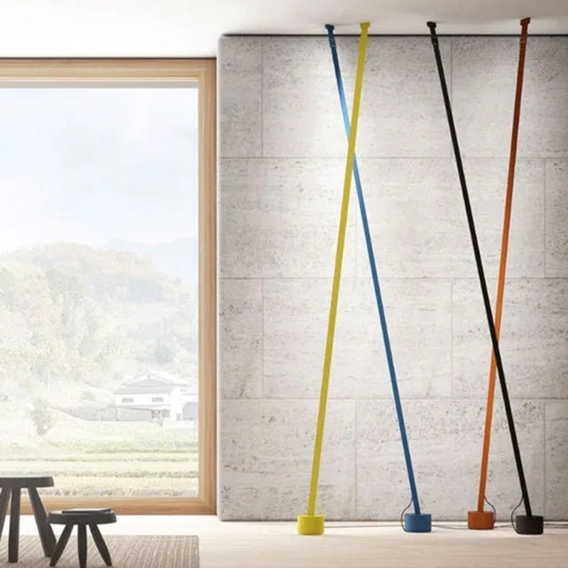 Yellow, blue, black and orange-brown Clérachic floor lamp strips lean against a stone wall beside a tall window with hills beyond.