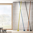 Yellow, blue, black and orange-brown Clérachic floor lamp strips lean against a stone wall beside a tall window with hills beyond.