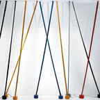 A row of black, ochre, blue, grey and red Clérachic floor lamp strips lean in front of a softly lit white wall.