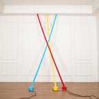 Three Clérachic floor lamp strips in light blue, yellow and red lean from the ceiling in front of a white panelled wall.